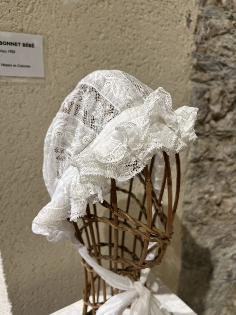 Exposition de dentelle dans l'ancienne église Saint-Gilles à Ambialet - bonnet de bébé en dentelle prêté par la société de location de costumes "Histoire en costumes" de Sérénac